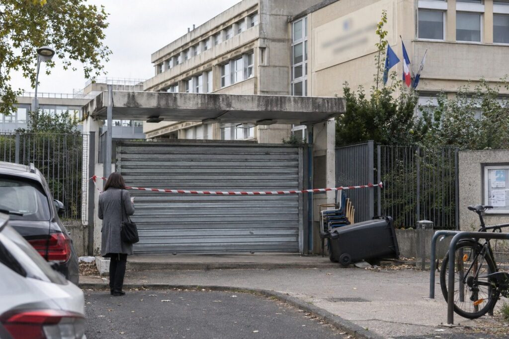 Portail métallique d'un lycée fermé, ruban de sécurité tendu, rue calme le matin