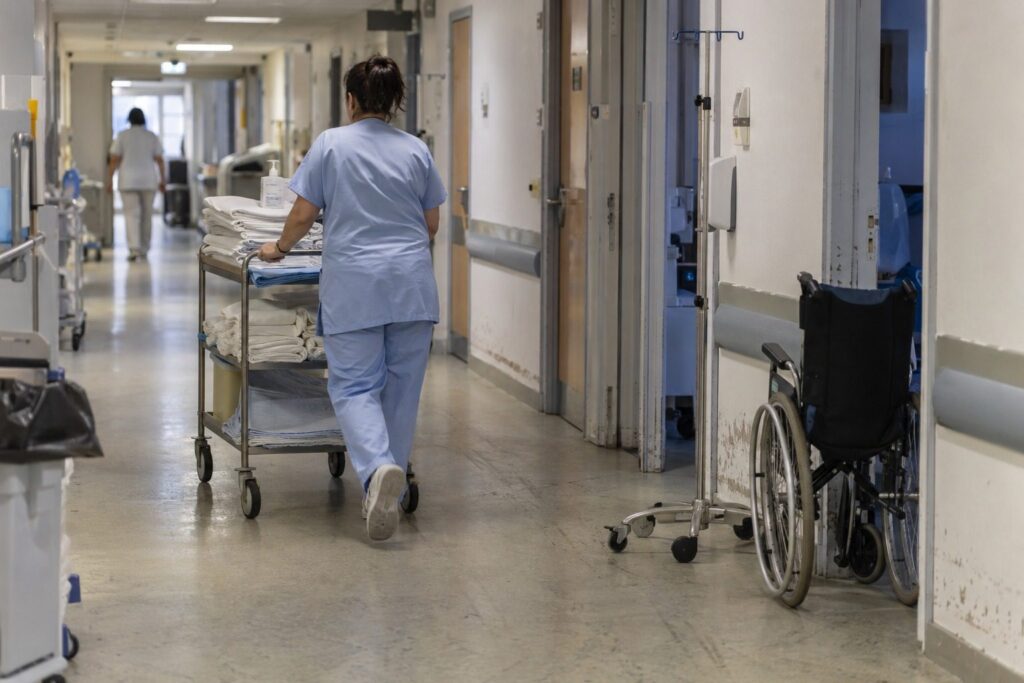Couloir d'hôpital avec un soignant poussant un chariot de soins entre les chambres